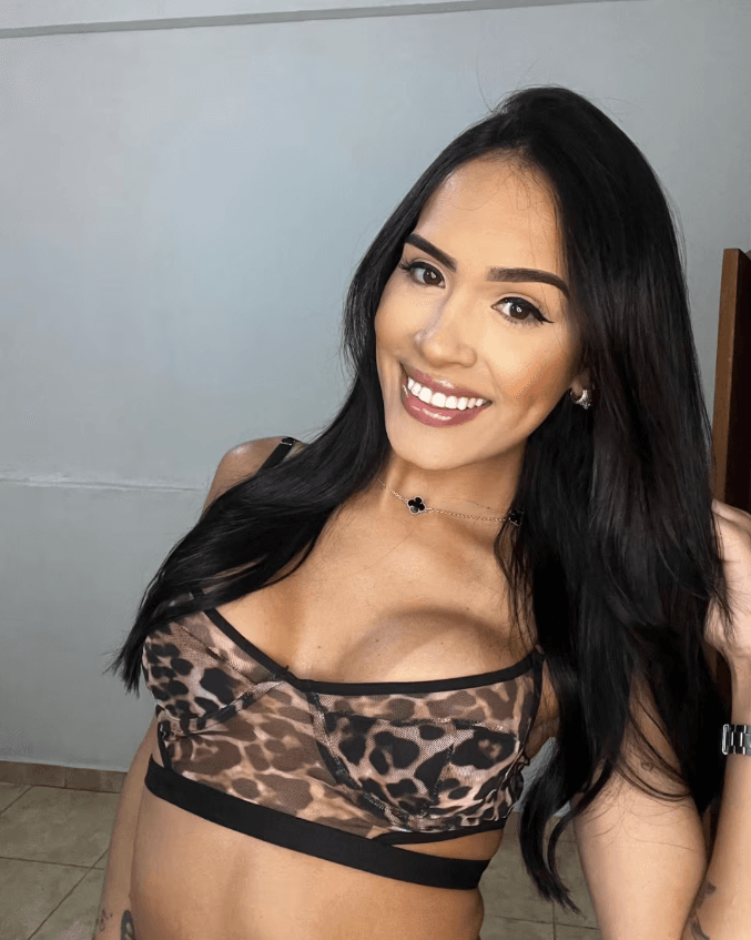 Smiling woman with long dark hair in a leopard-print bralette posing for a selfie.