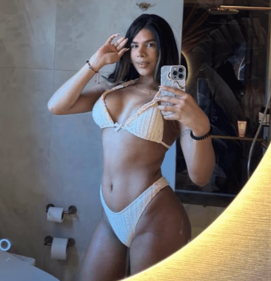 Woman in a white bikini taking a mirror selfie in a bathroom, holding a phone.