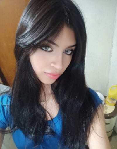 Close-up of a woman with long dark hair and blue eyes, wearing a blue top, looking at the camera.